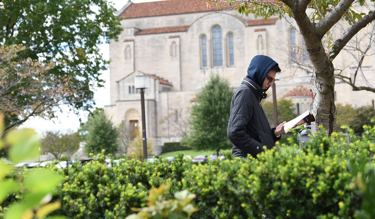 Second mosaic photo shows a male student reading a book as he walks along the University Mall with the Basilica of the National Shrine of the Immaculate Conception in the background. 
