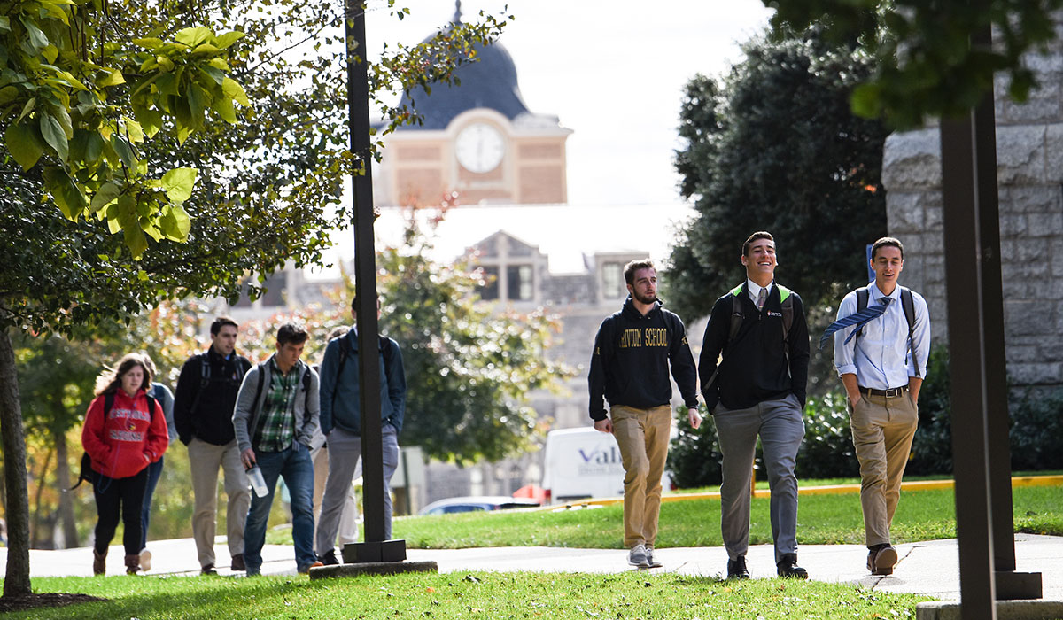 Fourth mosaic photo shows groups of students walking on the sidewalk beside McMahon Hall with the Monroe Street Market clock tower in the background.