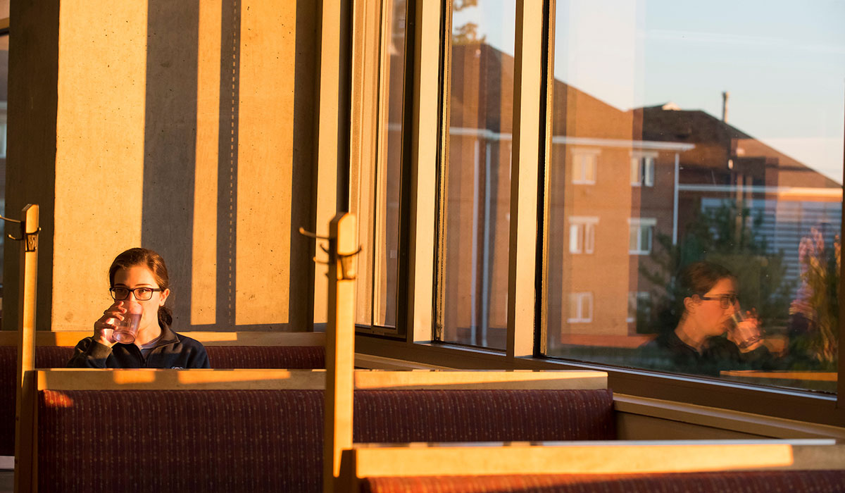 Seventh mosaic photo shows a female student seated in a booth in the student restaurant with a view of a residence hall through the window beside her.